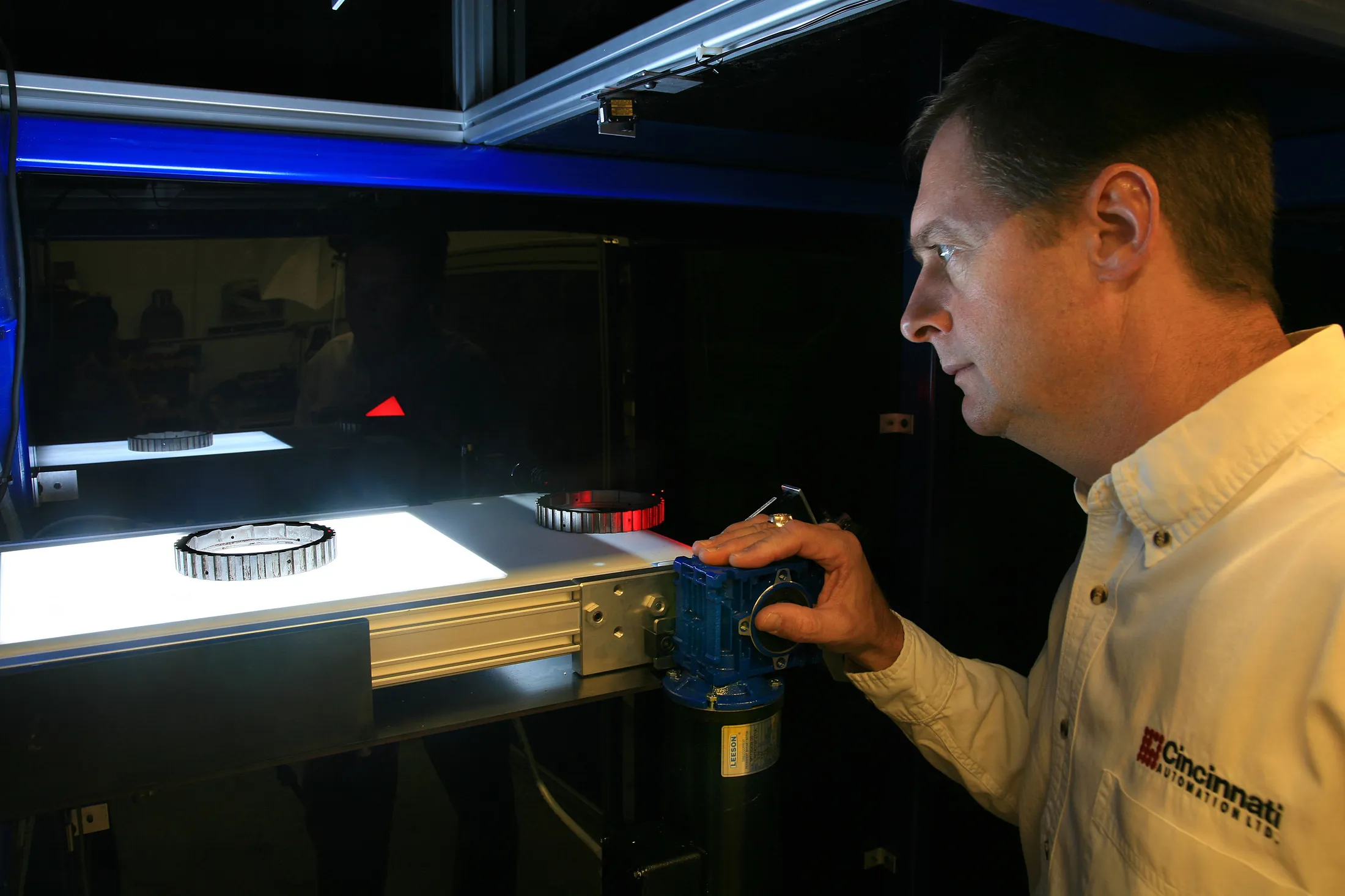 A person examining ring-shaped parts on a backlit conveyor inside inspection equipment.