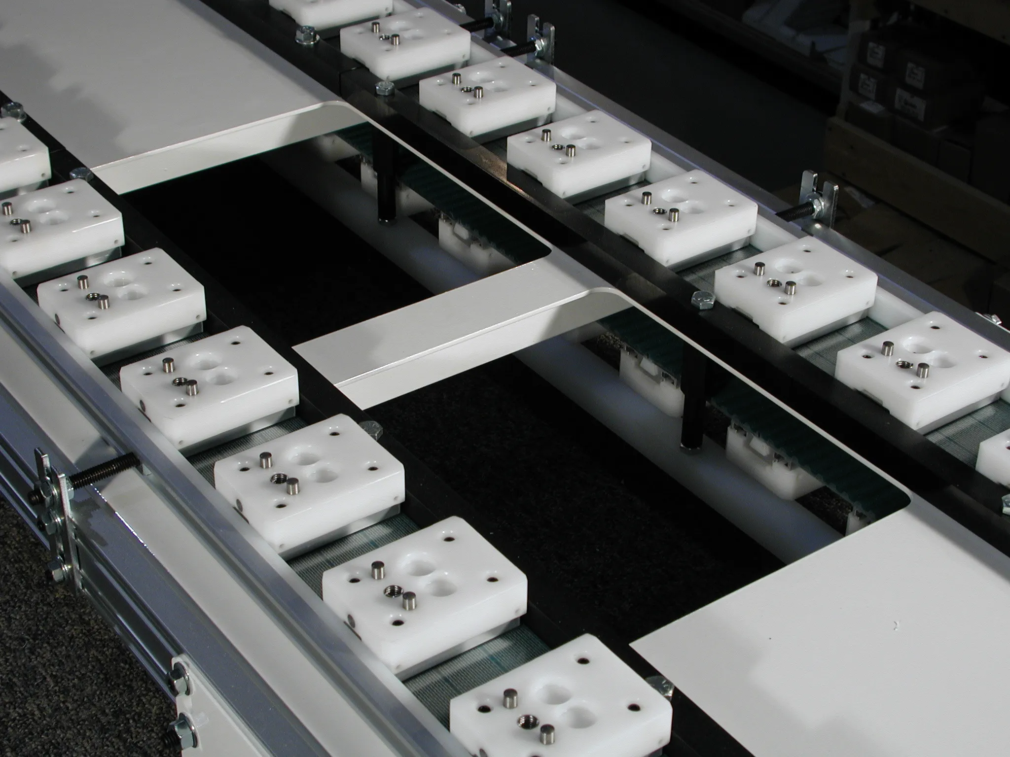 Locating pins on individual holders alongside plates spanning two conveyor belts.